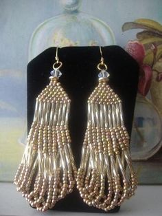 two pairs of gold colored beaded earrings on a black display stand next to a painting