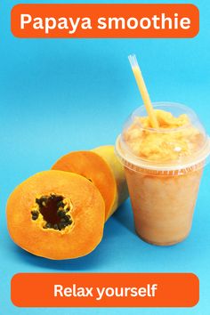 papaya smoothie in a plastic cup next to two pieces of fruit on a blue background