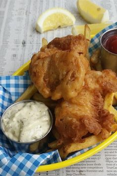 fried chicken and french fries with dipping sauces in a yellow bowl on a newspaper