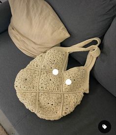 a crocheted purse sitting on top of a couch next to a pillow and pillows