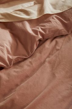 an unmade bed with pink sheets and pillowcases on top of each other