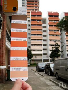 a hand holding up a color swatch in front of some buildings and cars on the street