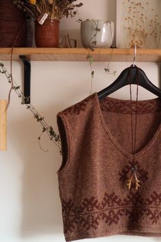 a brown sweater hanging on a wooden shelf next to plants and vases with dried flowers