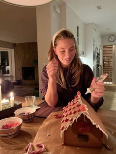 a woman sitting at a table in front of a gingerbread house with icing on it