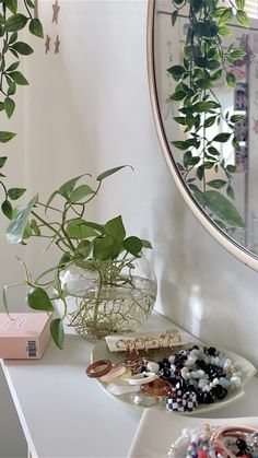 a white table topped with lots of plants next to a round mirror and jewelry tray