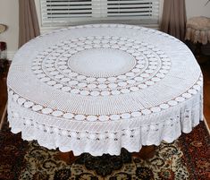 a round table with white crocheted doily on it in front of a window