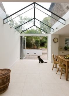 a black dog sitting in the middle of a room next to a table and chairs