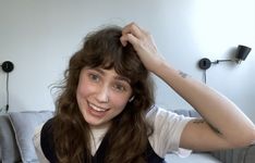 a woman with long hair is smiling and holding her head in one hand while sitting on a couch