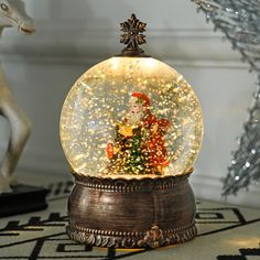 a snow globe with a christmas tree inside on a table next to a deer statue