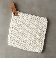 a white crocheted pot holder with leather handles on a gray surface, next to a pair of scissors