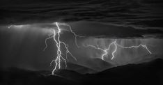 black and white photo of lightning striking over mountains