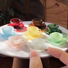 a person pointing at a small plate with cups on it and saucers in the middle