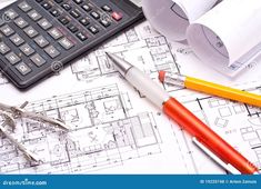 a calculator, pen and scissors on top of blueprints with rolls of paper