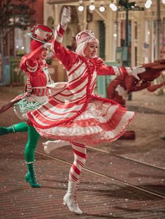 two women in red and white dresses are dancing on the street with lights behind them