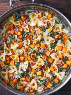 a pan filled with pasta and vegetables on top of a wooden table