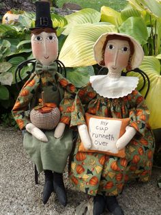 two scarecrow dolls sitting next to each other in front of some plants and flowers