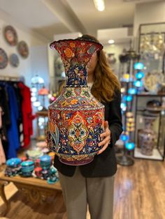 a woman is holding a large vase in her hands and looking at the camera while she shops