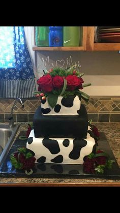 a three tiered cake decorated with red roses and black cow print, on top of a kitchen counter