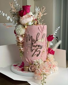 a pink cake decorated with flowers and writing on the top is sitting on a table