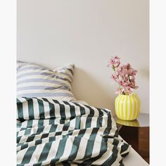 a vase with pink flowers sitting on top of a bed next to pillows and blankets