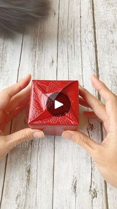 two hands holding a red square object with a video playing button on the front side