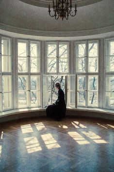 a woman sitting on top of a window sill in front of a chandelier