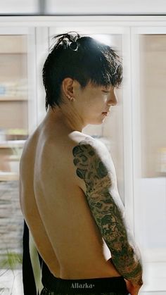 a man with tattoos on his arm and shoulder standing in front of a window looking at something