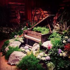 an old piano is surrounded by flowers and rocks