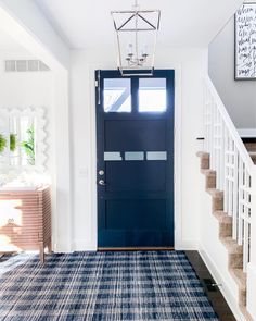 a blue front door and stairs in a white room with rugs on the floor