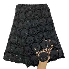 a woman's hand is holding up a black lace skirt with flowers on it