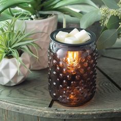 a candle that is sitting on a table next to some potted plants and greenery