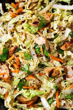 a salad with chicken, carrots and lettuce in a black bowl on a table