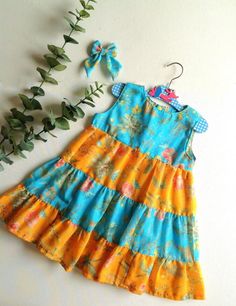 a blue and yellow dress sitting next to a green leafy plant on top of a white surface