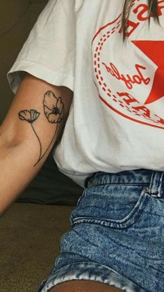 a woman with a flower tattoo on her arm sitting down and looking at the camera