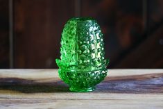 a green glass candle holder sitting on top of a wooden table next to a wall