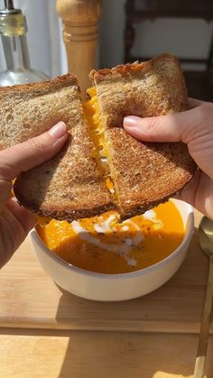 two hands holding a sandwich over a bowl of soup