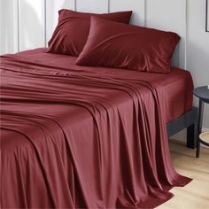 a bed with red sheets and pillows on it in a room next to a table