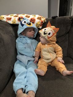 two babies in costumes sitting on a couch