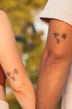 two people holding hands with tattoos on their arms and one has a heart in the shape of a map