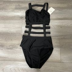 a women's black swimsuit with straps on the bottom and side, sitting on a wood floor