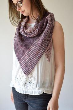 a woman wearing glasses and a purple knitted shawl over her shoulder, standing in front of a white wall