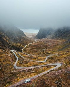 an aerial view of a winding road in the mountains with fog and low lying grass