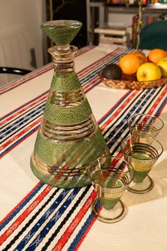 there are three glasses on the table with fruit in the backgroung behind them