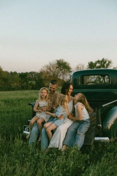 a group of people sitting on the back of an old truck in a grassy field