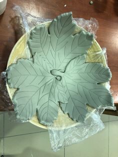 a plate with leaves on it sitting on top of a wooden table next to plastic wrap