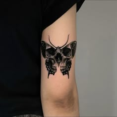 a black and white photo of a butterfly tattoo on the right arm, with a skull in the middle