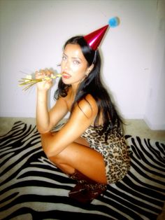 a woman sitting on top of a zebra print rug wearing a party hat and holding flowers