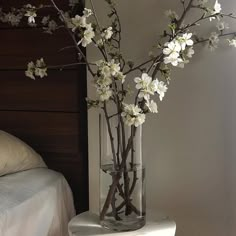 there is a vase with white flowers in it on the table next to a bed