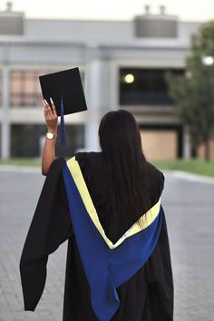 a woman in graduation gown holding up a black and blue square with a yellow stripe