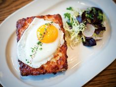 a white plate topped with meat and an egg on top of it next to a salad